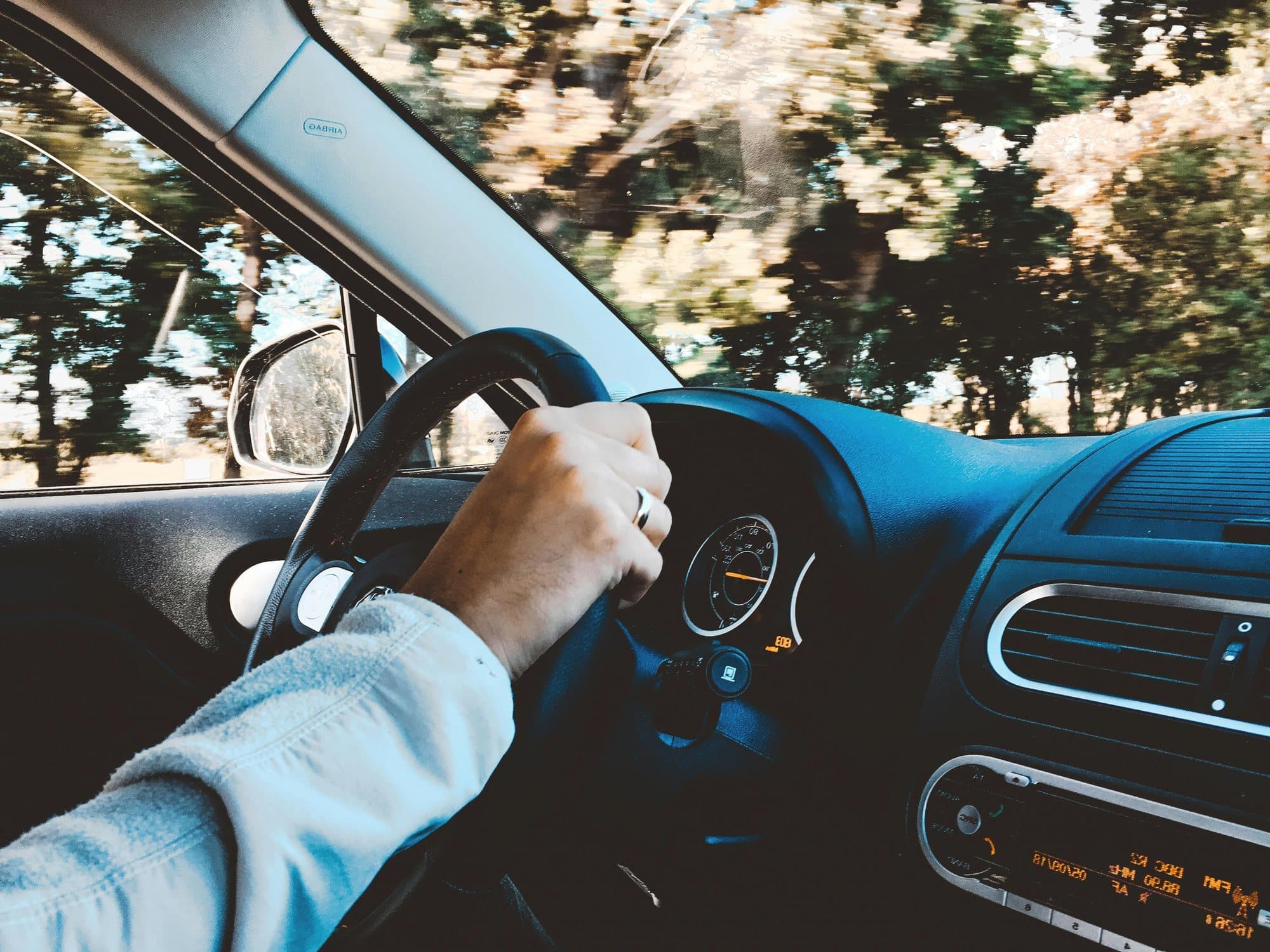 A driver's hand on the wheel on a tree-lined road, from the instructor's seat